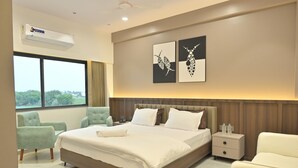 Ein modernes Hotelzimmer mit einem großen Bett, zwei Sesseln, einem Nachttisch und Kunstwerken an der Wand.