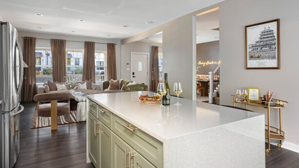 A modern kitchen with a large island, wooden cabinets, and a dining area with a sofa and table. - The Nowland Reserve |Sauna, Arcade, Sleeps 14 (Indianapolis)