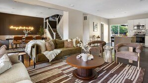 A modern living room with a staircase, a dining area, and a kitchen. - The Nowland Reserve |Sauna, Arcade, Sleeps 14 (Indianapolis)