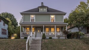 A two-story house with a front porch, a chimney, and a small front yard. - The Nowland Reserve |Sauna, Arcade, Sleeps 14 (Indianapolis)