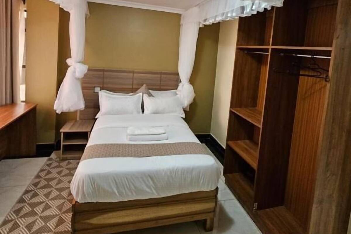 A hotel room with a bed, a bedside table, a wardrobe, and a patterned rug.