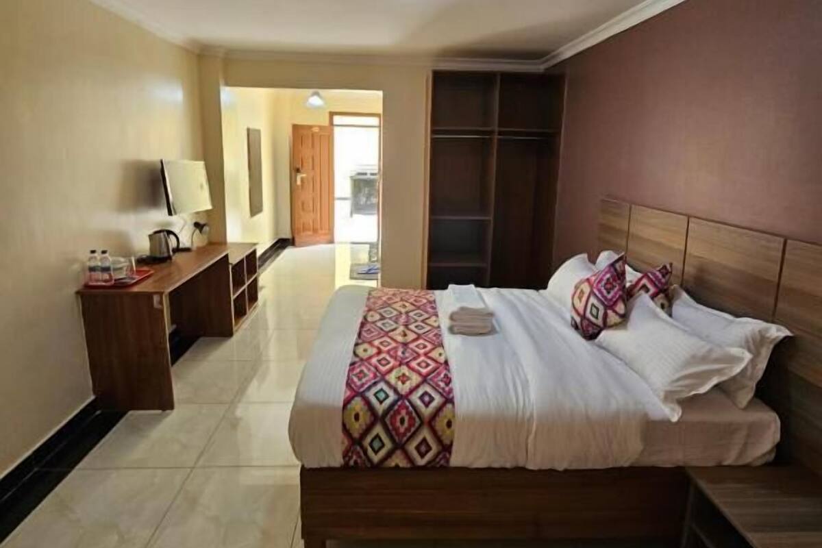A hotel room with a bed, bedside table, and a desk with a lamp.