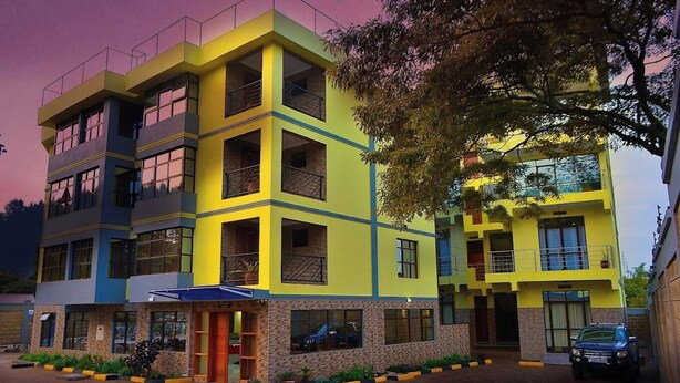 A multi-story building with a yellow and blue facade, featuring balconies and a brick base.