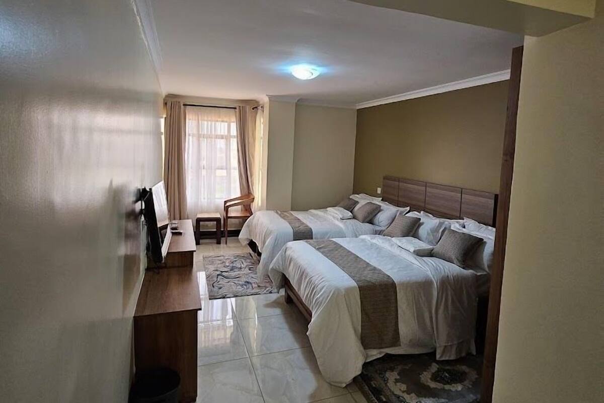 A hotel room with two beds, a desk, a chair, and a window with curtains.