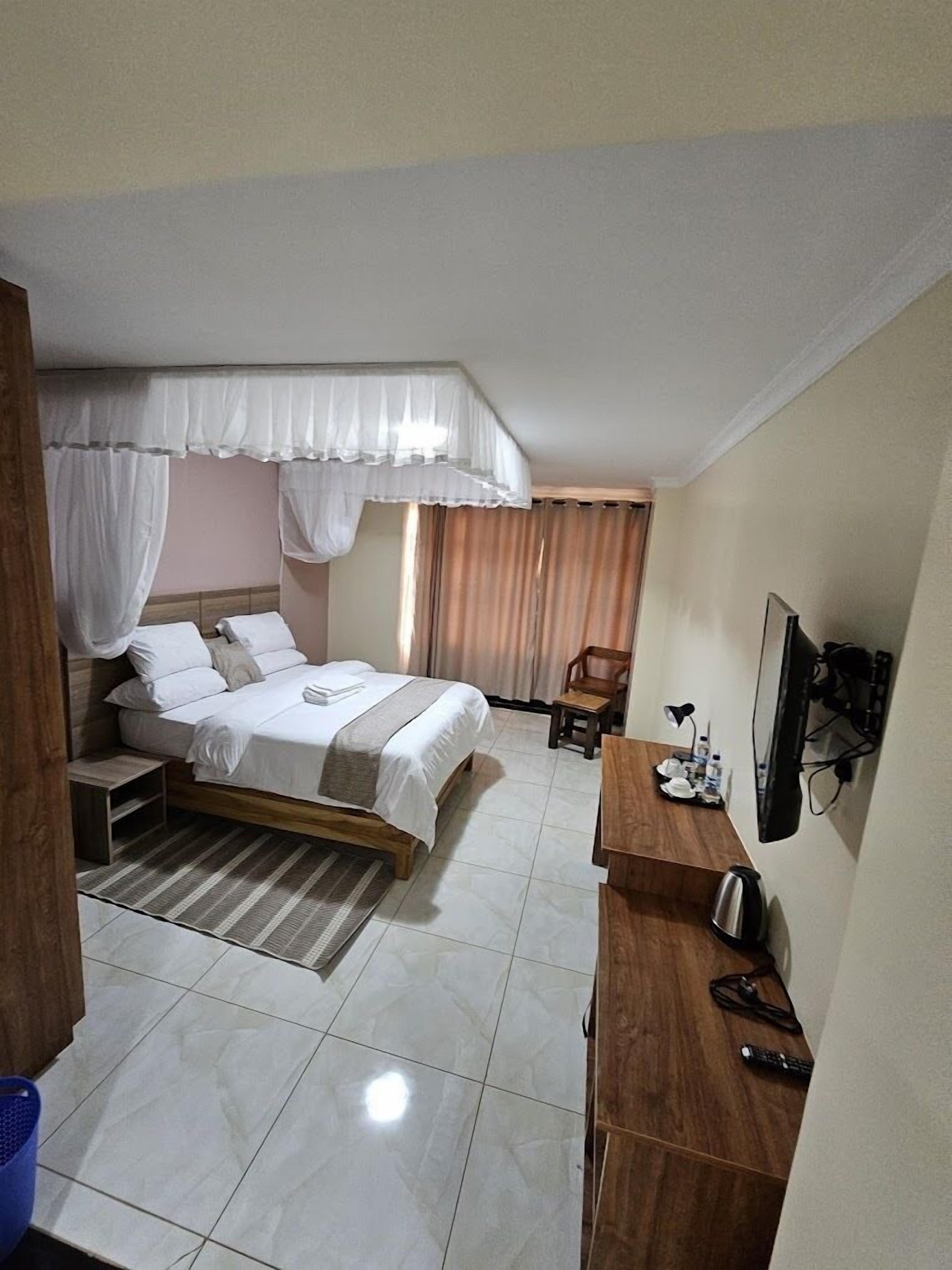 Un dormitorio con cama, escritorio, silla, televisor y ventana con cortinas.