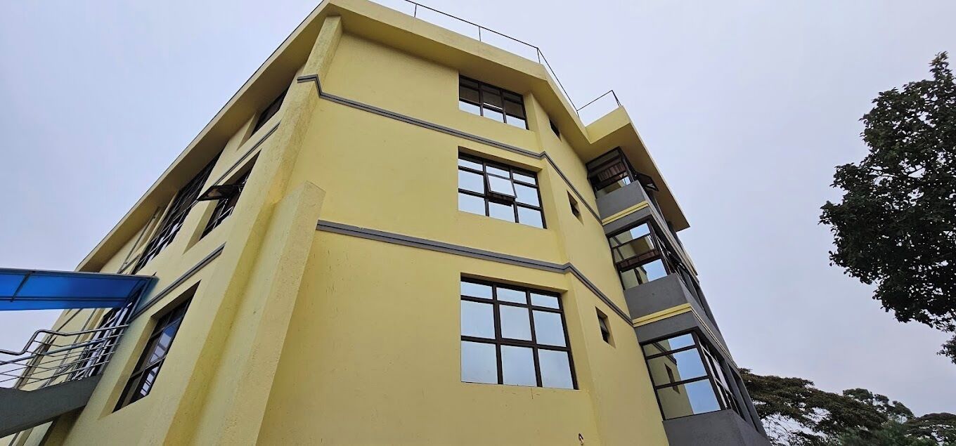 A multi-story building with a yellow facade, large windows, and a blue structure to the left.