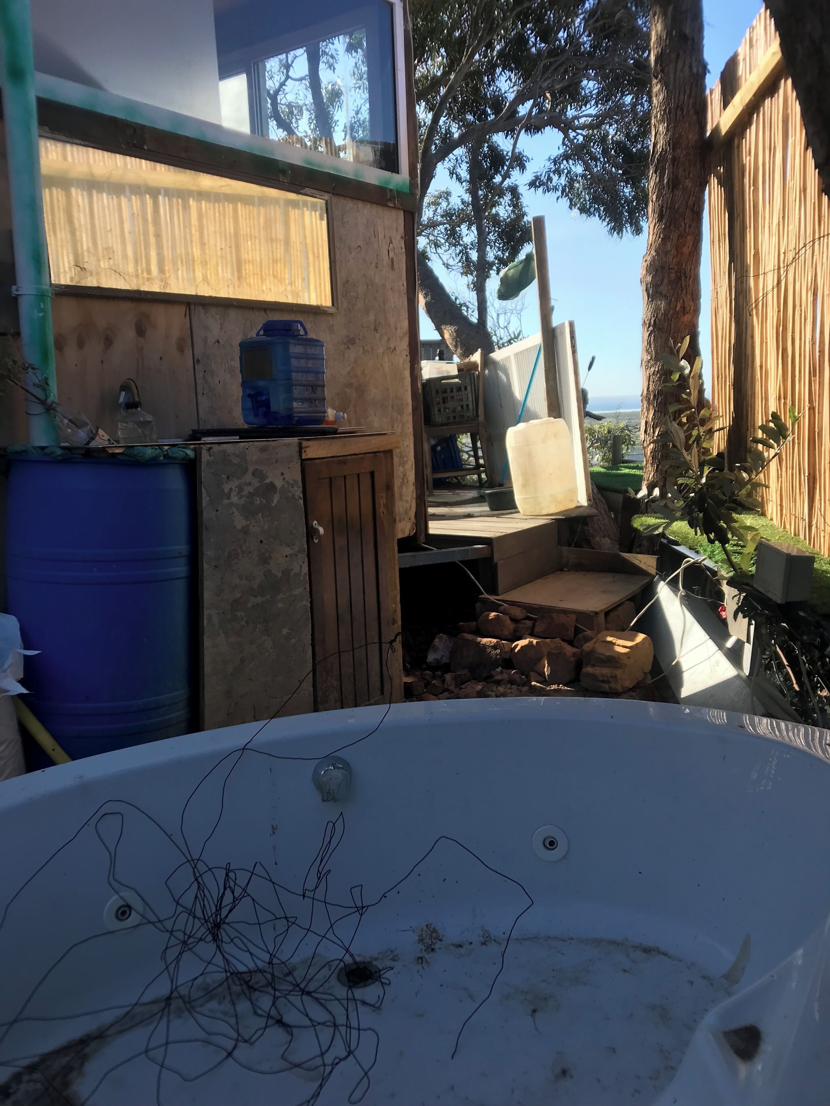 A rustic outdoor area with a wooden deck, a hot tub, and various items like a water cooler and a bicycle.