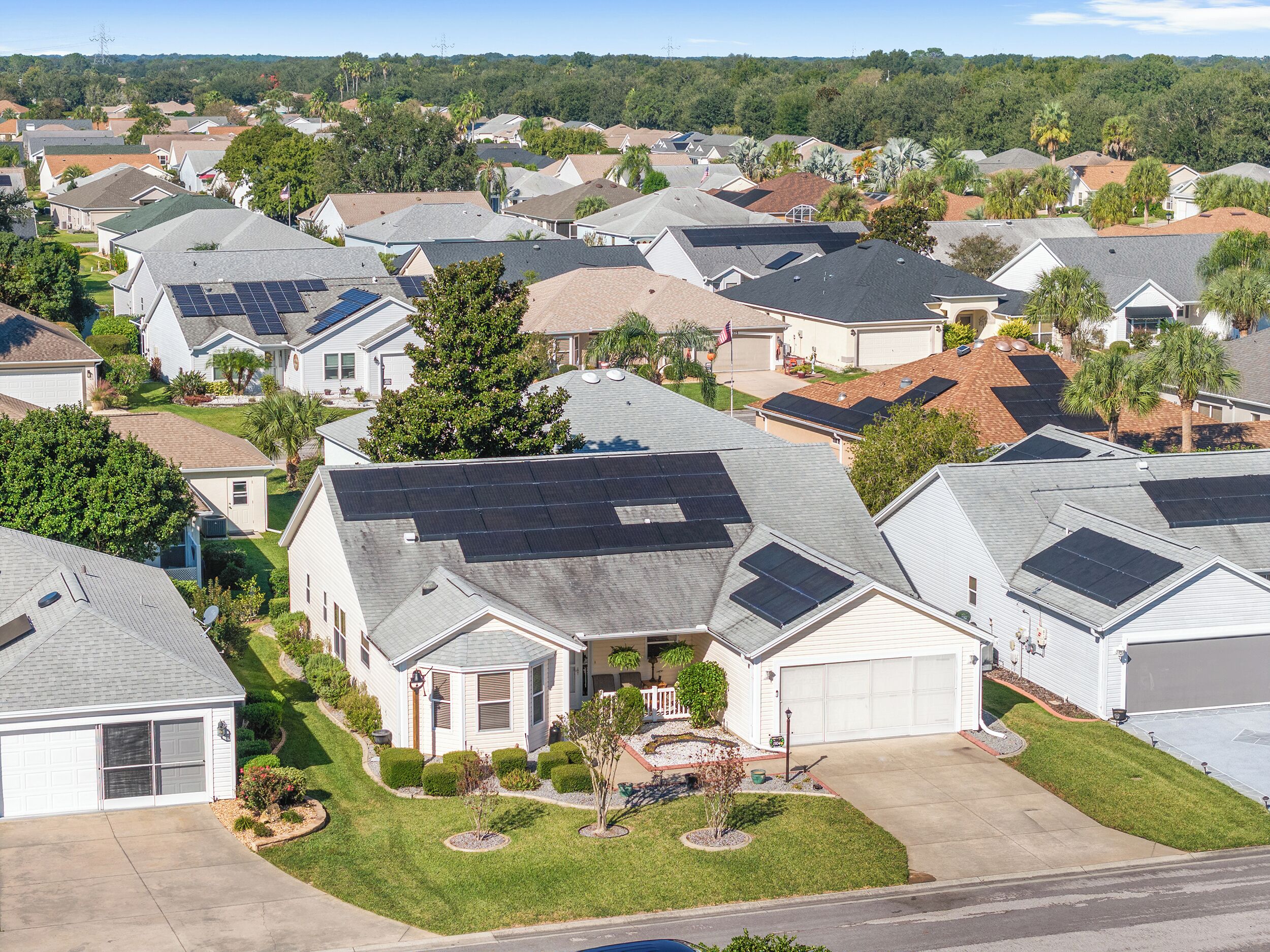 A residential area with houses featuring solar panels, well-maintained lawns, and a suburban neighborhood layout.