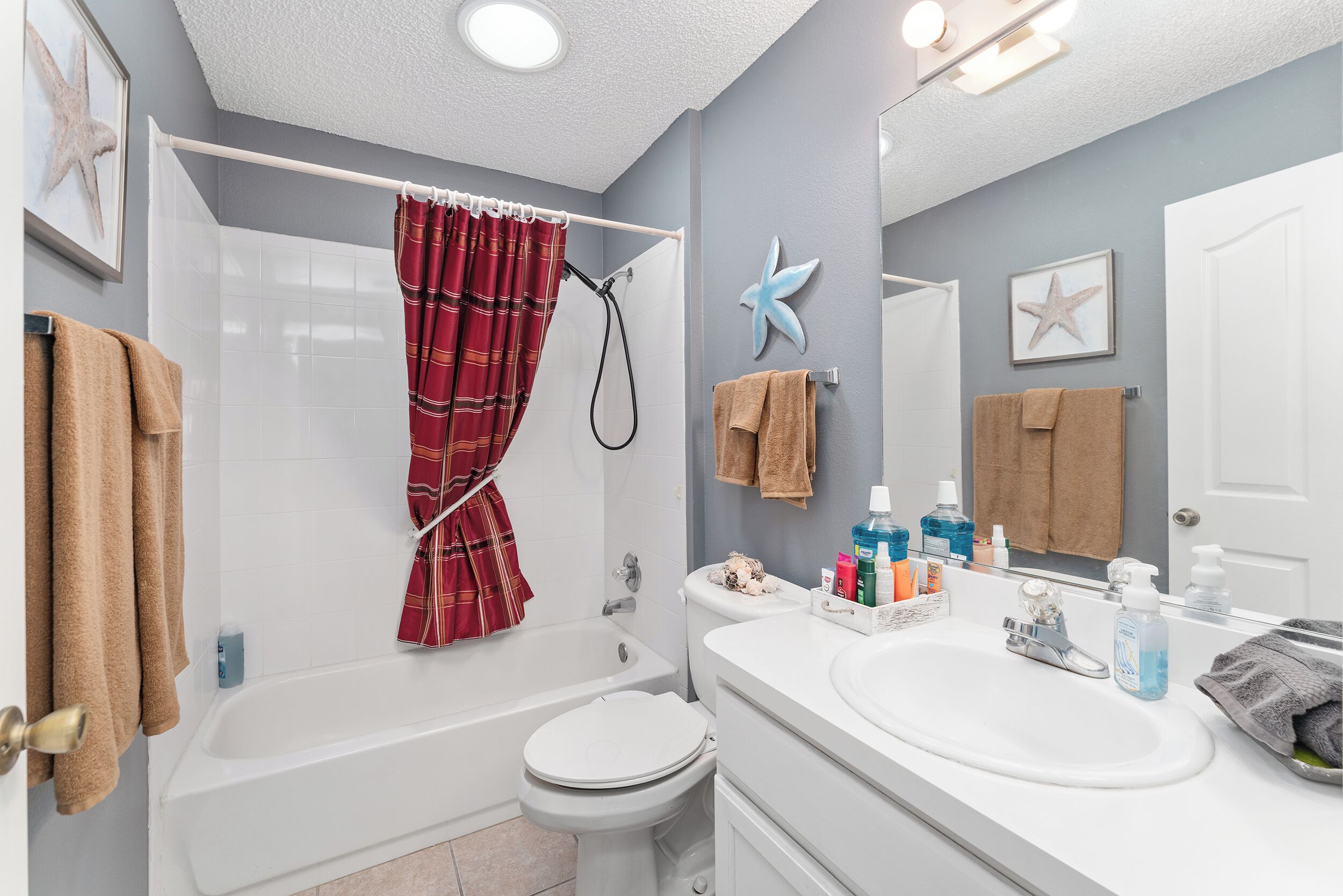 Une salle de bain avec une baignoire, des toilettes et un lavabo. On y trouve des serviettes, des articles de toilette et une étoile de mer décorative accrochée au mur.
