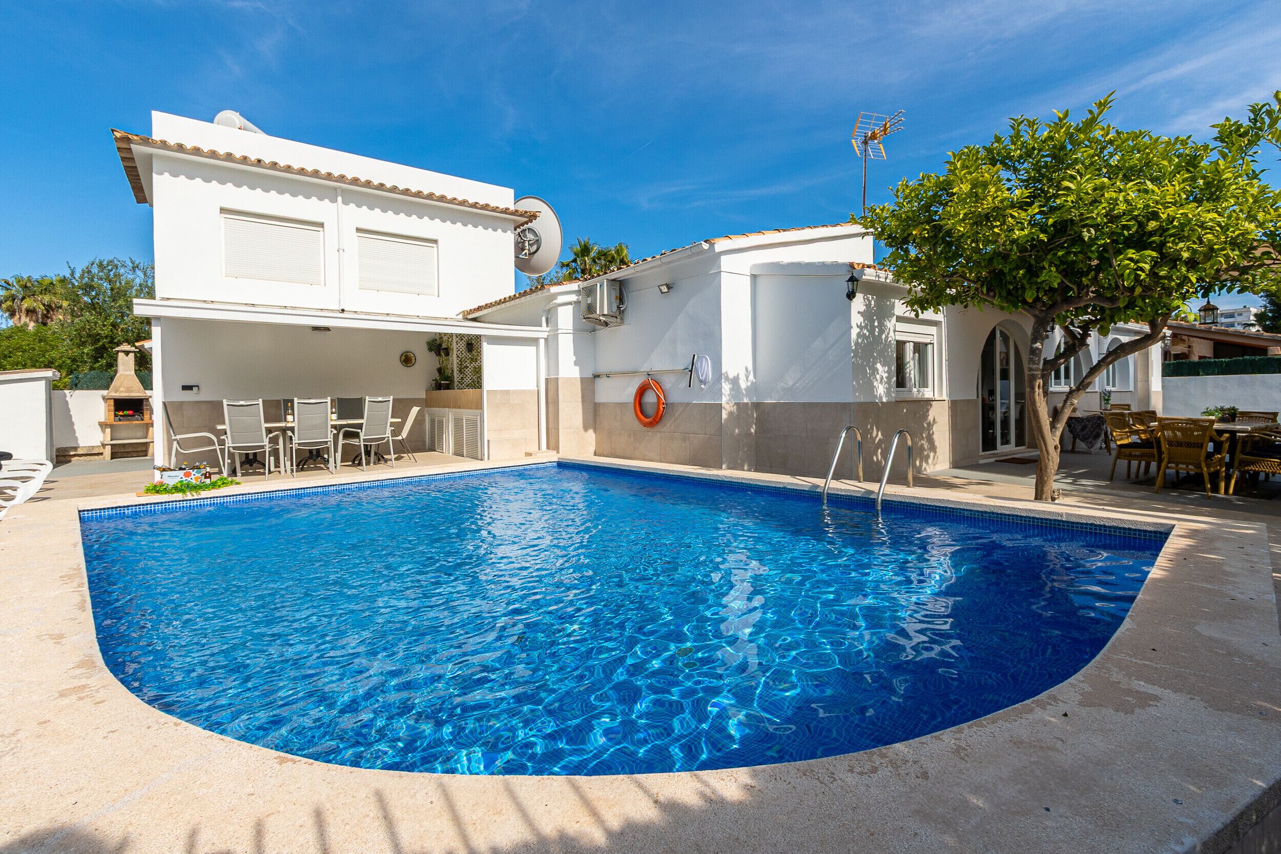 A swimming pool with a curved edge, surrounded by a patio area with chairs and a table.