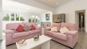 A spacious living room with two pink sofas, a white coffee table, and a large window providing natural light. - Villa Casa Blanca in Alcudia by Home Villas 360 (Alcúdia)