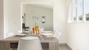 A dining area with a wooden table set for four, white chairs, and a bottle of wine. - Villa Casa Blanca in Alcudia by Home Villas 360 (Alcúdia)