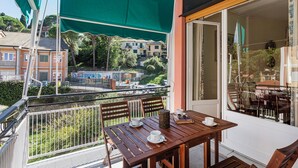 Ein Balkon mit einem Holztisch und Stühlen, einem grünen Markisenstoff und Blick auf Gebäude und Grünflächen im Hintergrund.