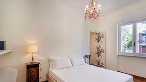 Ein Schlafzimmer mit Bett, Sessel, Nachttisch, Lampe, Fenster und Tür, verziert mit Blumenmuster.