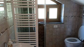 Ein Badezimmer mit einer Duschkabine, einem Waschbecken, zwei Toiletten und einem Fenster über der Dusche.