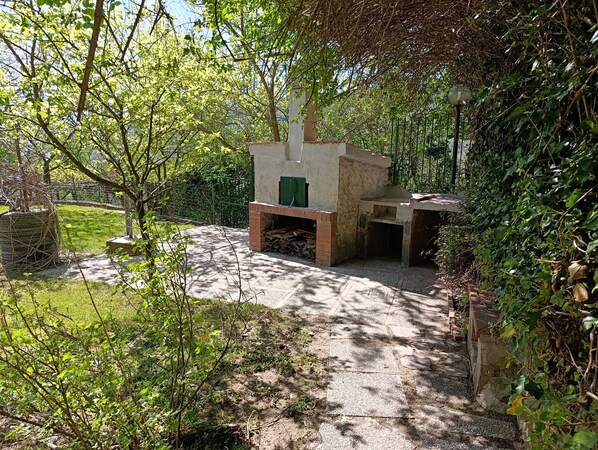 A garden area with a stone bench, a small structure with a green door, and a pathway leading through it.