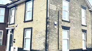A two-story brick building with white-framed windows, a satellite dish, and a small attached garage. - Corner Stone House Apartment 2 (Great Yarmouth)