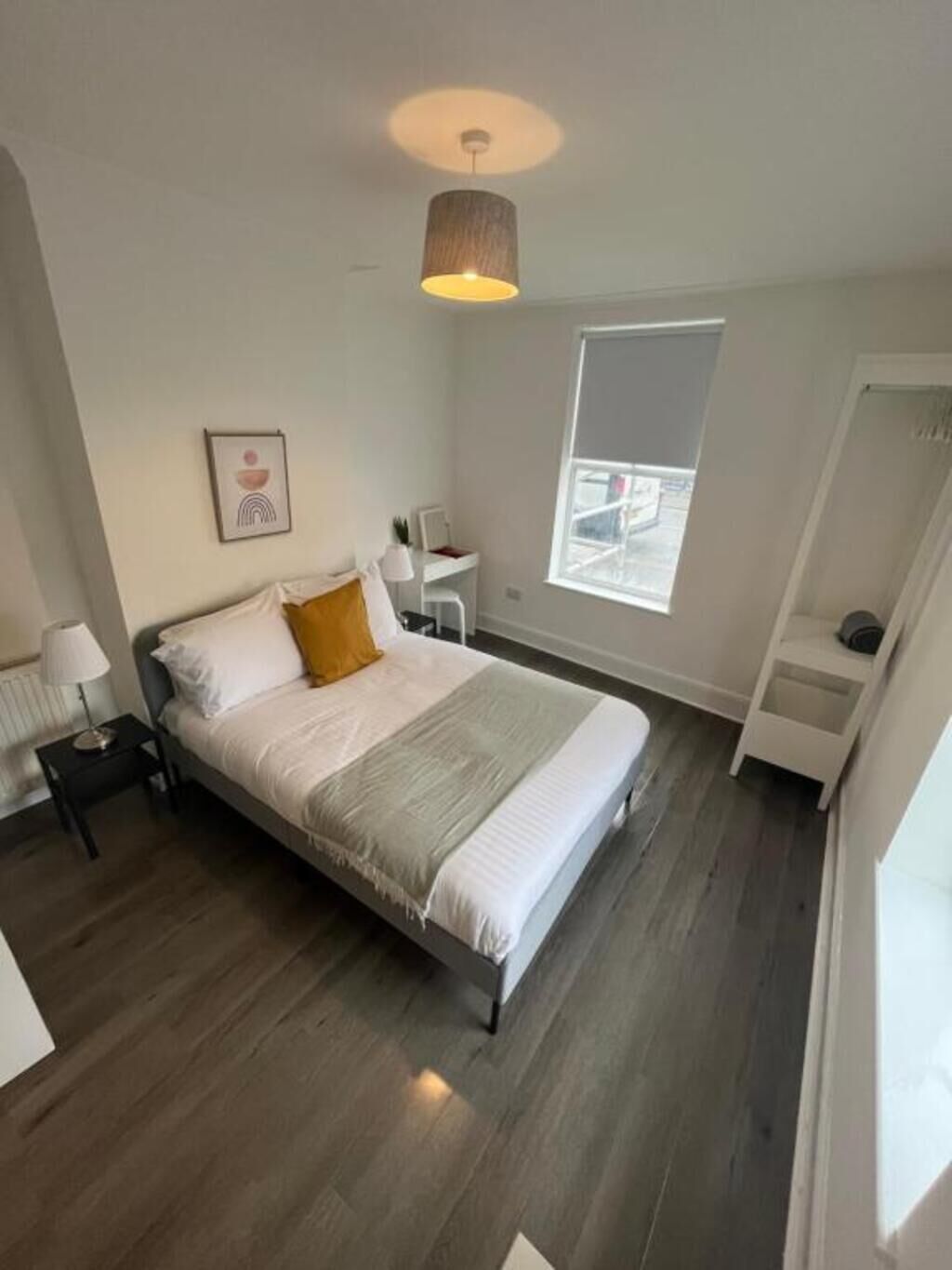 Ein Schlafzimmer mit Bett, Nachttisch, Schreibtisch, Stuhl, Fenster und einer Pendelleuchte.