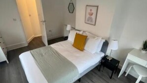 A bedroom with a large bed, bedside tables, a desk, and a hanging light fixture. - Corner Stone House Apartment 2 (Great Yarmouth)
