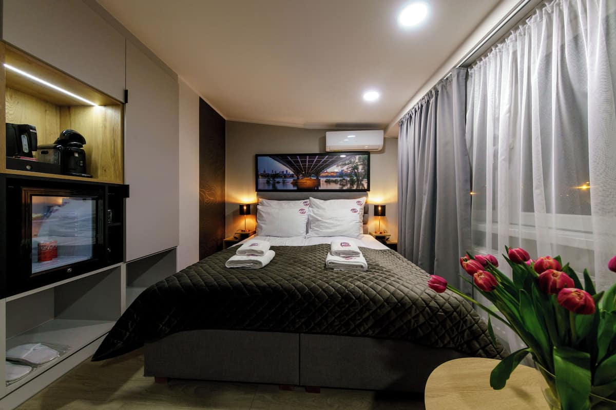 Una camera d'albergo moderna con un letto grande, una televisione a schermo piatto, una macchina del caffè e vista sulla città dalla finestra.