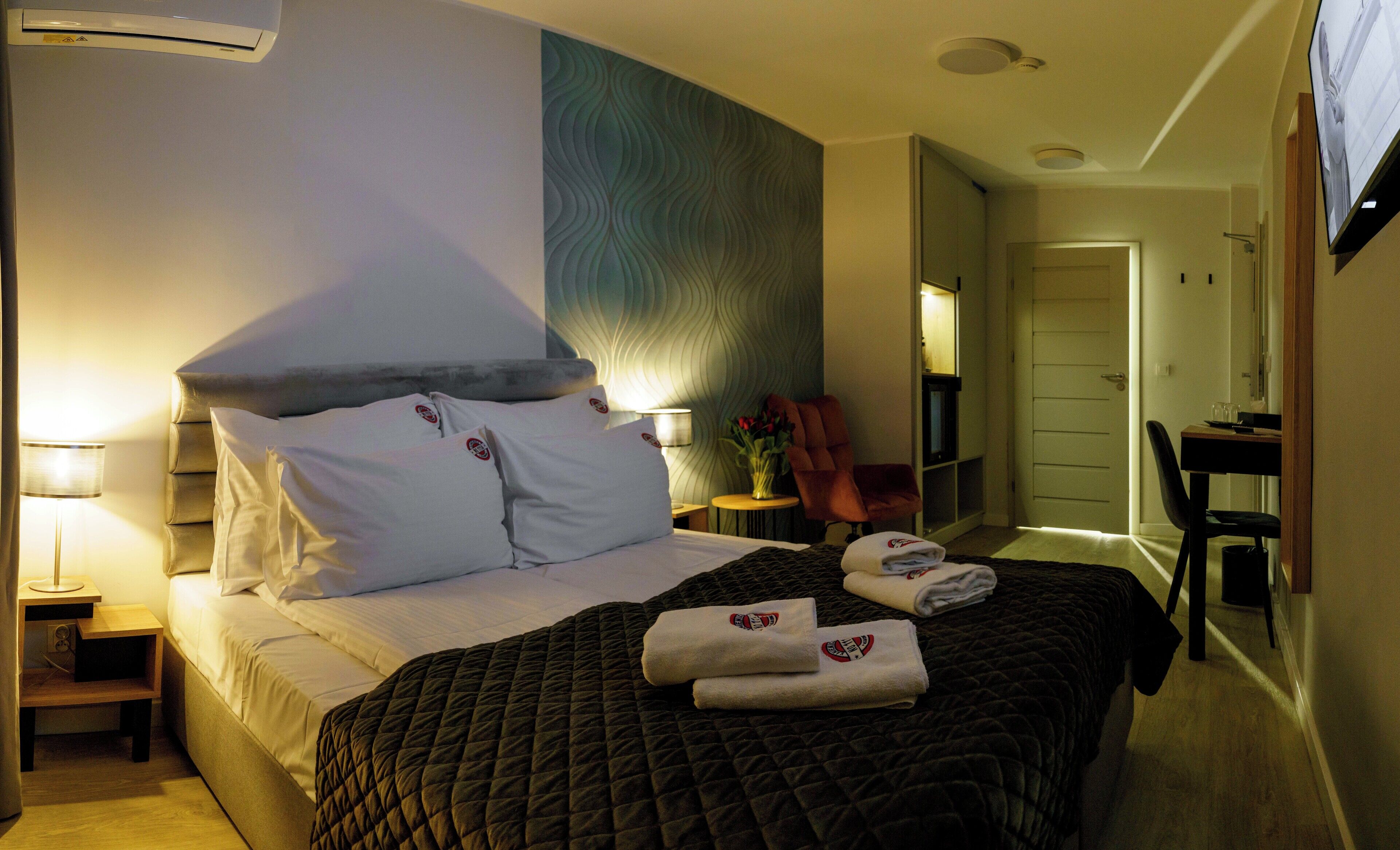 A hotel room with a bed, a nightstand, a chair, a desk, and a TV.