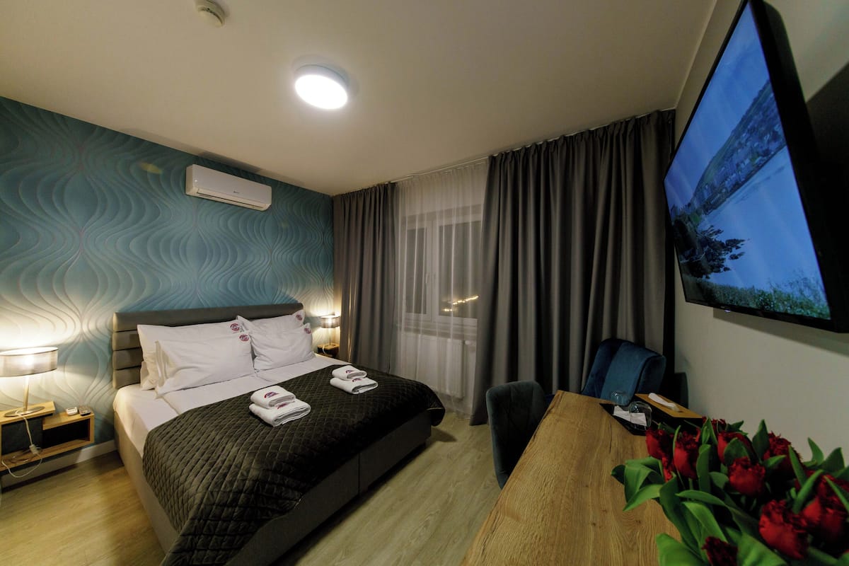Una camera d'albergo con un letto, una scrivania, una televisione e una finestra con tende.