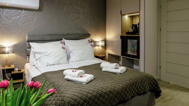 A modern hotel room with a large bed, a bedside table, a lamp, and a wall-mounted air conditioner. - Kamienica no111a (Warsaw)