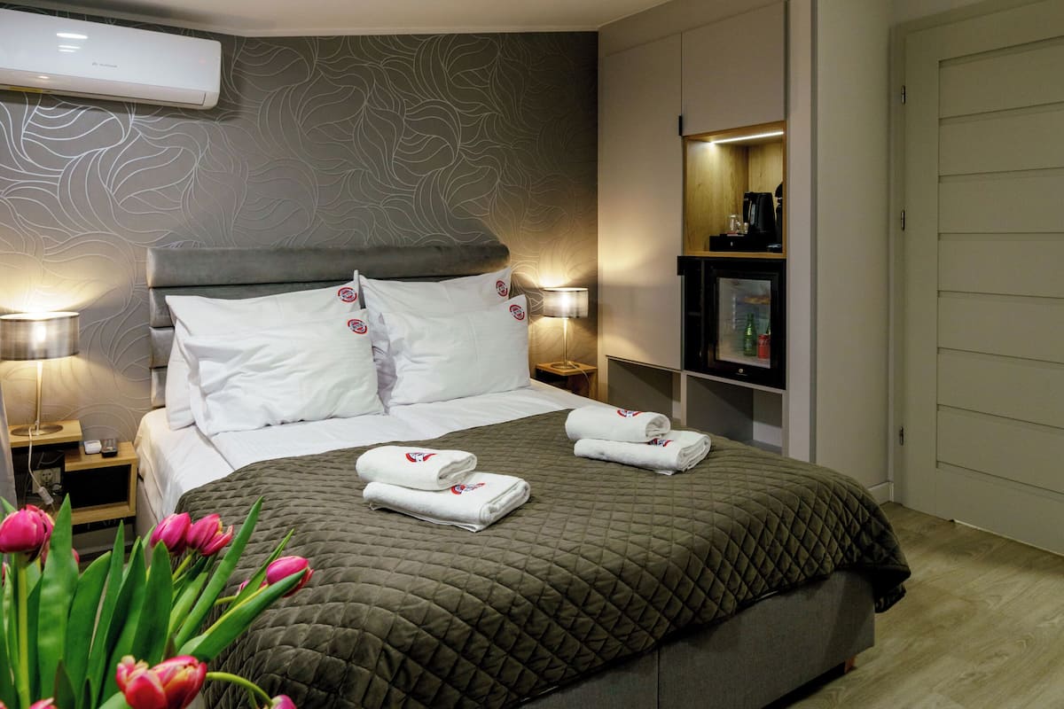 Una moderna camera d'albergo con un letto grande, un comodino, una lampada e un condizionatore d'aria a parete.