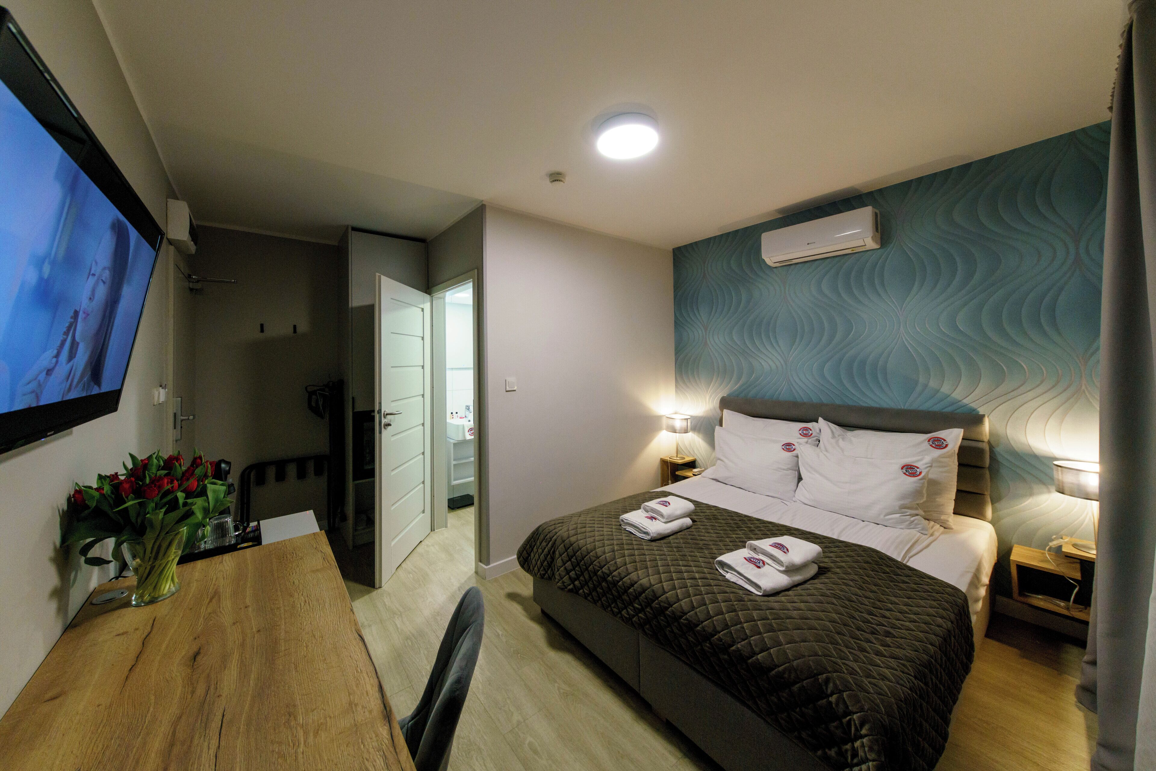 Una habitación de hotel con cama, mesitas de noche, televisor y un florero.