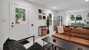 Ein modernes Wohnzimmer mit Ledersofa, Couchtisch und Essbereich, im Hintergrund eine Küche.