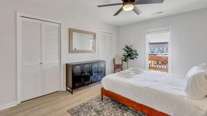 Ein Schlafzimmer mit Bett, Deckenventilator, Kommode, Spiegel und Blick ins Freie.