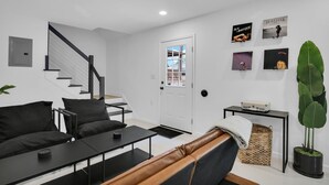 Ein modernes Wohnzimmer mit Treppe, einer Couch, einem Couchtisch und einer großen Pflanze.