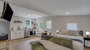 A modern hotel room with a kitchenette, a bed with two pillows, a bedside table with a lamp, and a sofa. - Cypress Cottage - Cozy Lake Getaway (Shad Moss village)
