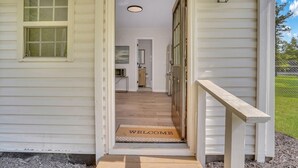 A house entrance with a wooden door, a welcome mat, and a view into the interior. - Cypress Cottage - Cozy Lake Getaway (Shad Moss village)