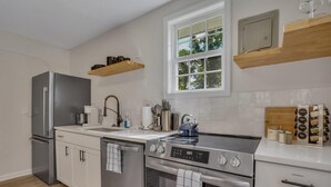 A modern kitchen with stainless steel appliances, wooden shelves, and a window providing natural light. - Cypress Cottage - Cozy Lake Getaway (Shad Moss village)