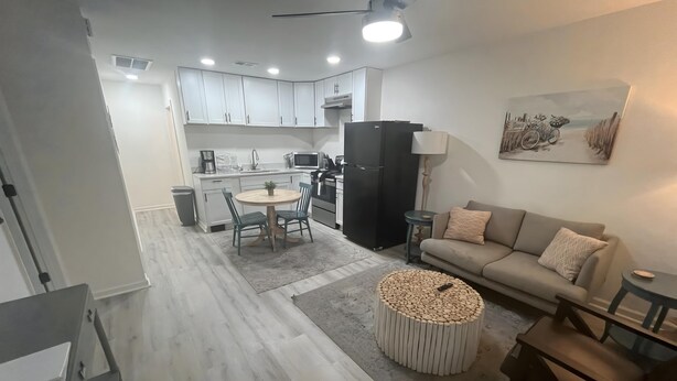 Una cocina moderna con armarios blancos, un comedor con una mesa redonda y una sala de estar con un sofá y una mesita de centro.