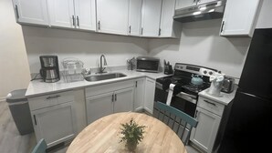 Una cocina compacta con alacenas blancas, un lavamanos, un microondas, una estufa y un refrigerador.