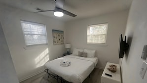 Un dormitorio con cama, mesita de noche, lámpara y ventilador de techo.