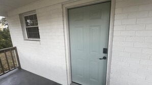Fachada de ladrillo blanco con una puerta cerrada, una ventana pequeña y un porche de hormigón.