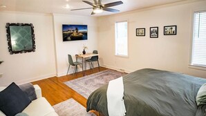 A bedroom with a bed, a desk with chairs, a ceiling fan, and framed pictures on the wall. - The Palmetto Place - 2br Modern Unit on Remount (North Charleston)