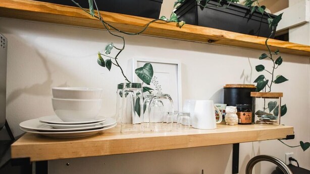 A kitchen counter with stacked white plates, clear glass jars, a white mug, and a small white figurine. - The Palmetto Place - 2br Modern Unit on Remount (North Charleston)