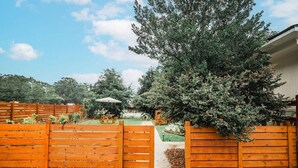 A wooden fence with a garden area, a patio, and a building in the background. - The Palmetto Place - 2br Modern Unit on Remount (North Charleston)