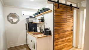 A compact kitchen with a wooden sliding door, white cabinetry, and a small countertop. - The Palmetto Place - 2br Modern Unit on Remount (North Charleston)