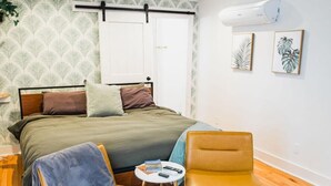 A bedroom with a bed, two chairs, a small table, and a ceiling fan. - The Grove Studio - Comfort in Style on Remount (North Charleston)