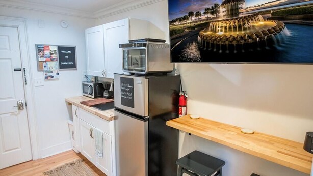 A compact kitchen with white cabinets, a microwave, a refrigerator, and a wooden shelf. - The Grove Studio - Comfort in Style on Remount (North Charleston)
