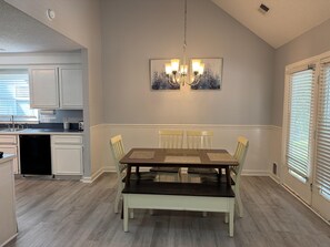 A dining area with a wooden table and chairs, a chandelier, and artwork on the wall.