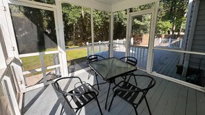 A covered patio with a table and chairs, a white railing, and a view of a backyard with a wooden deck and trees. - Bright & Roomy 4BR/5-Bed Home Just Off Dorchester (North Charleston)