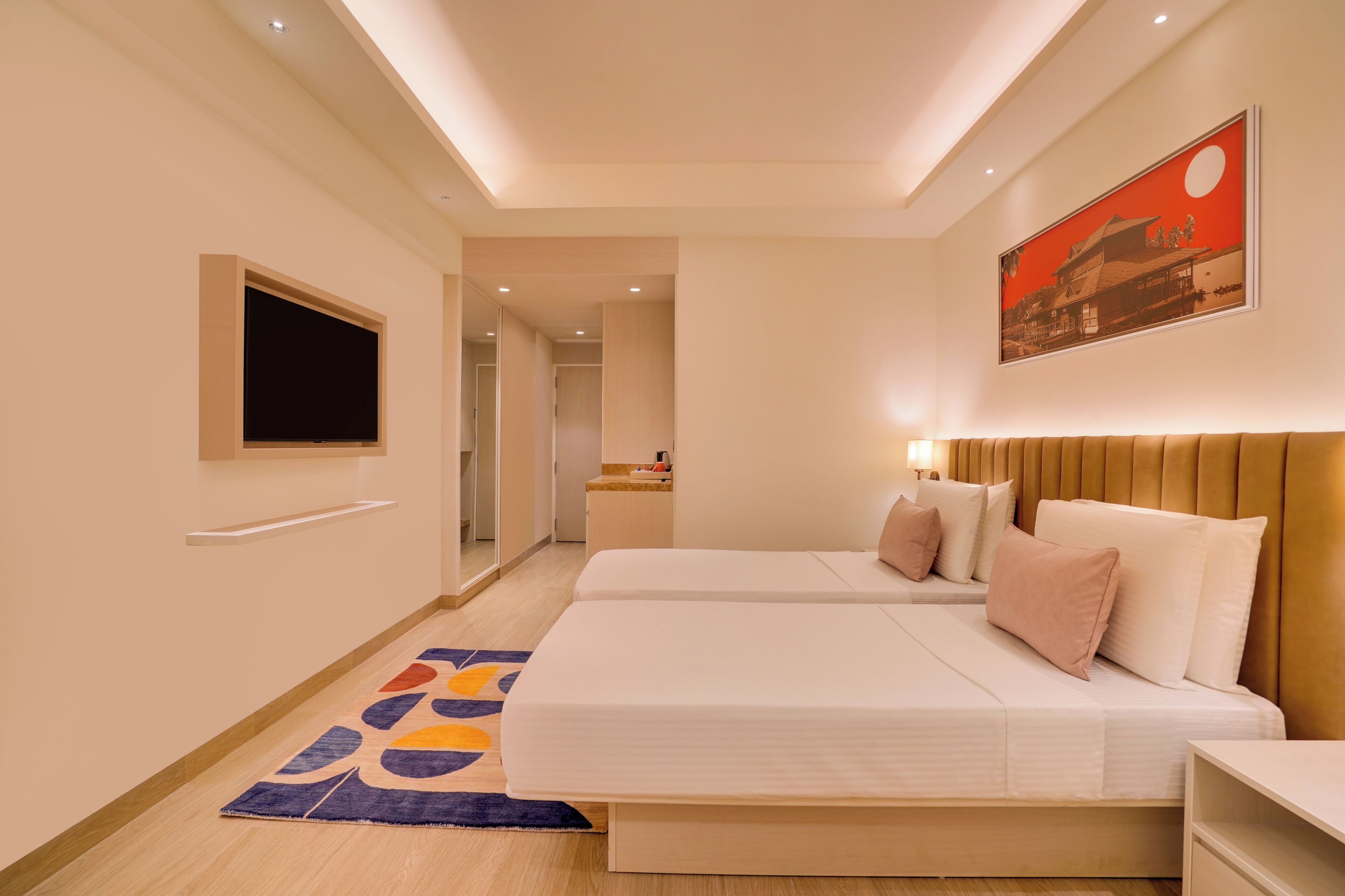 A hotel room with two beds, a TV, a painting, and a hallway leading to another room.