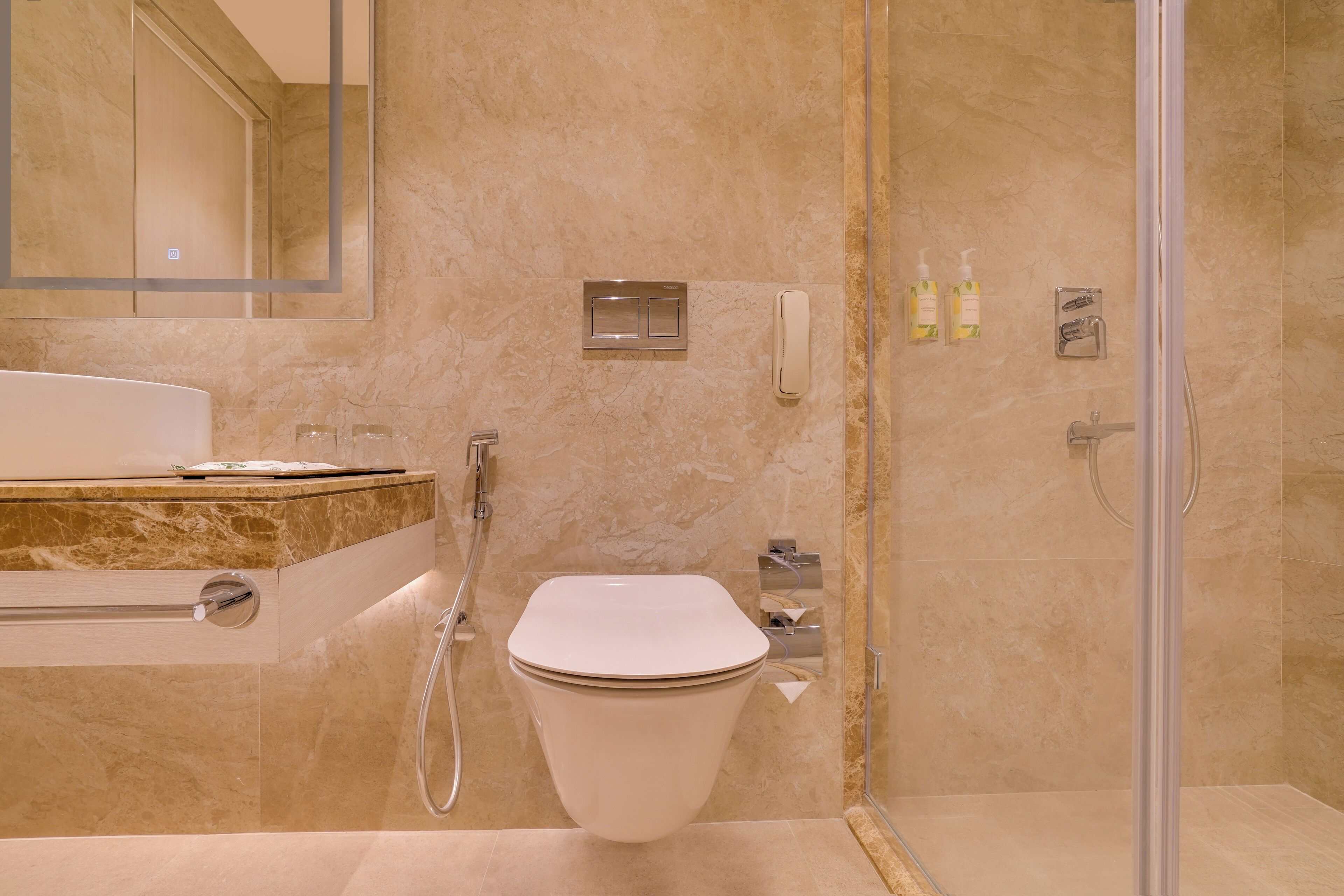 A modern bathroom with a marble floor, a white toilet, a glass-enclosed shower, and a vanity with a marble countertop.