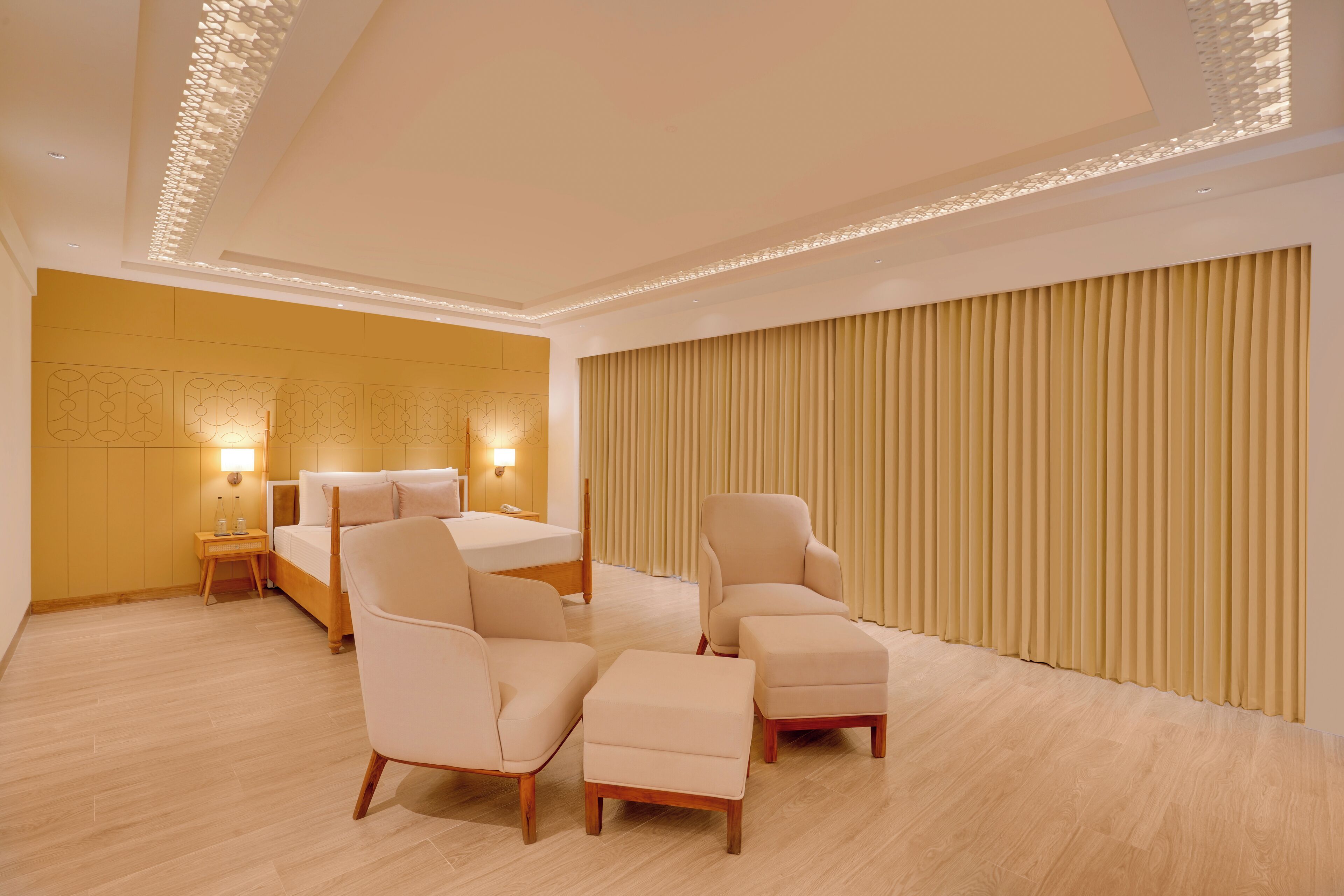 A modern hotel room with a large bed, two armchairs, a small table, and a wall-mounted TV.